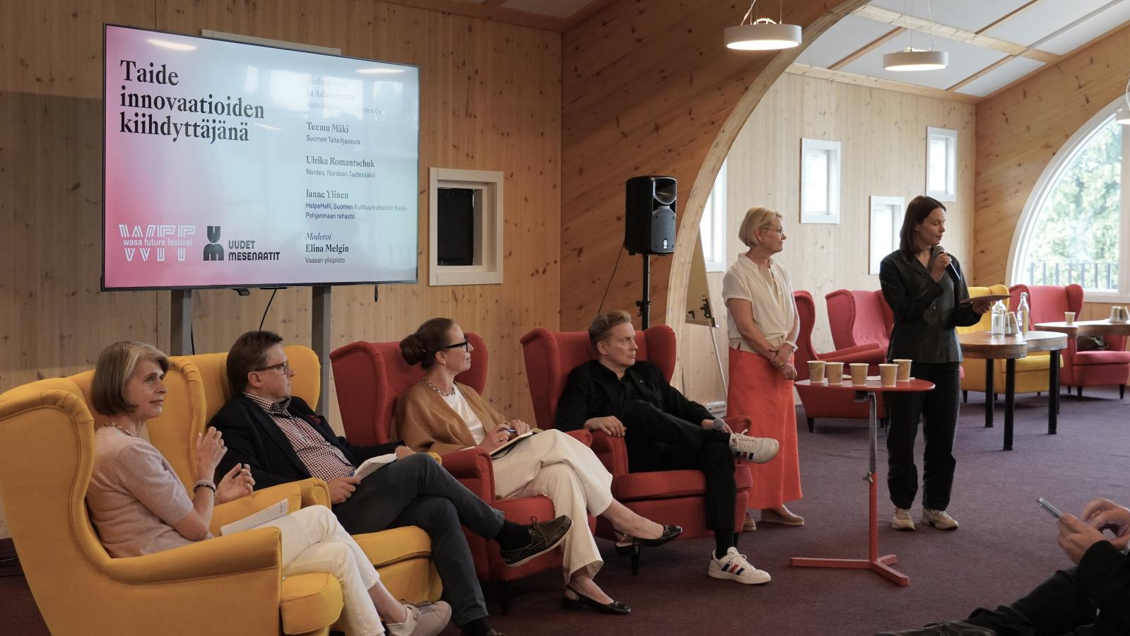 Ihmisiä paneelikeskustelussa. Taka-alalla näytöllä lukee Taide innovaatioiden kiihdyttäjänä. 