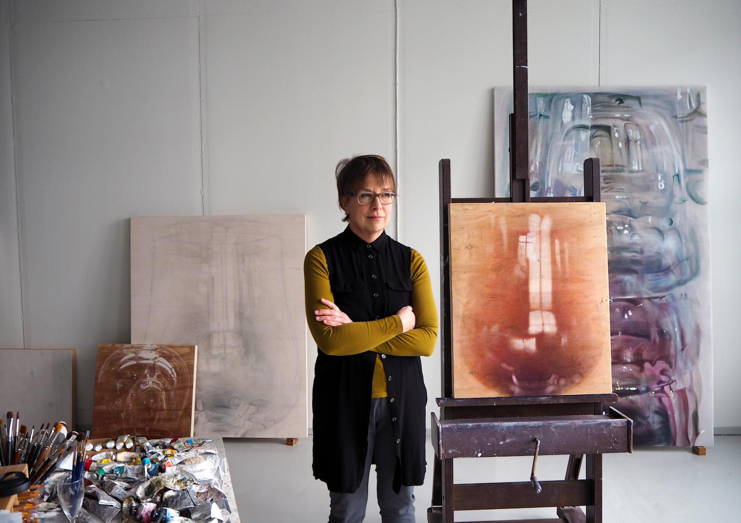 Kuvataiteilija Susanne Gottberg seisoo työhuoneessaan maalausten ympäröimänä.