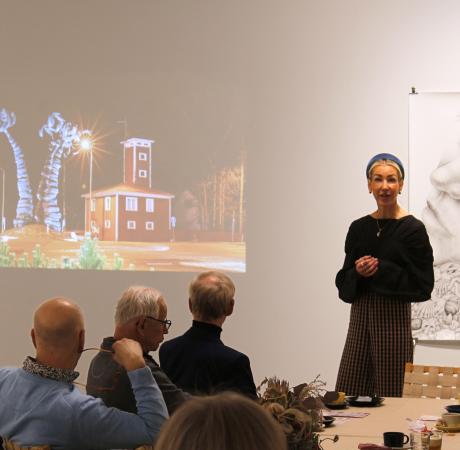 Vaaleahiuksinen naisoletettu pitää puheenvuoroa yleisön edessä