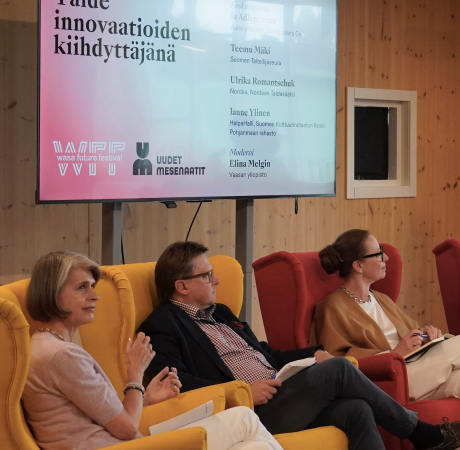 Kolme henkilöä istuu nojatuoleilla, taustalla teksti taide innovaatioiden kiihdyttäjänä